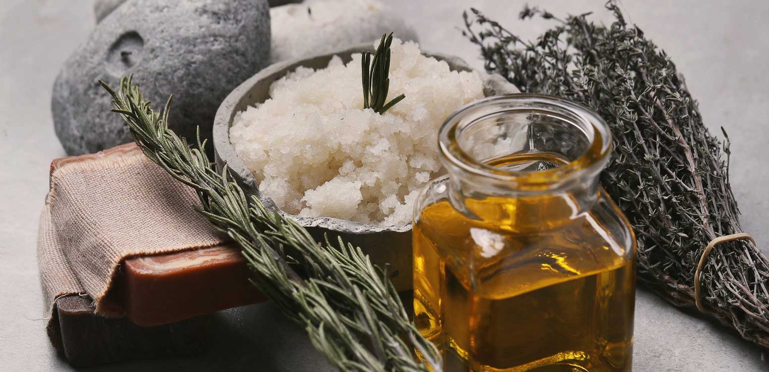 Spa arrangement with rosemary, salt, soap, and a bottle of essential oil, set on a rustic surface.